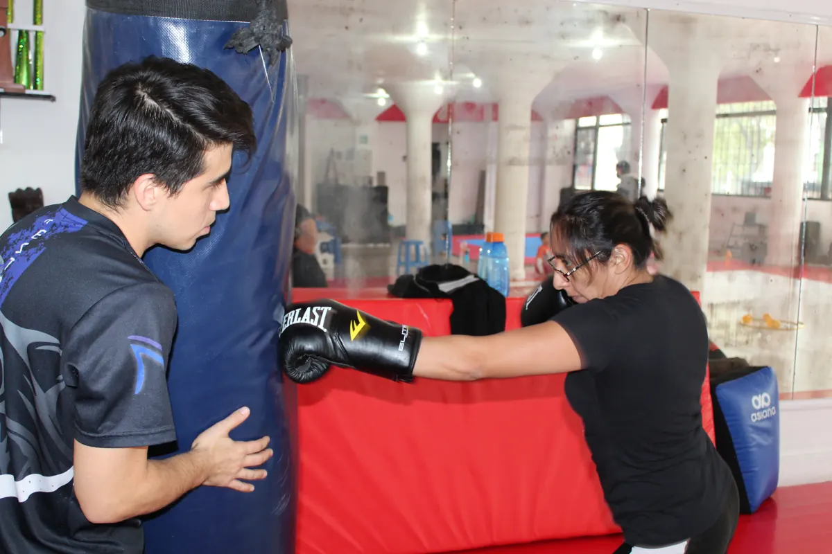 Entrenador corrigiendo técnica en el costal a una alumna de Fitness Training